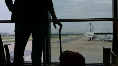 Solo gezgin havaalanı penceresinin yanında bavuluyla bekliyor, pistteki uçaklara bakıyor, macera beklentisini yakalıyor. Gezgin şehveti, havaalanı sahneleri, seyahat anları..