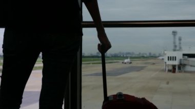 Solo gezgin havaalanı penceresinin yanında bavuluyla bekliyor, pistteki uçaklara bakıyor, macera beklentisini yakalıyor. Gezgin şehveti, havaalanı sahneleri, seyahat anları..