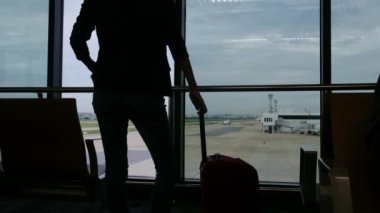Solo gezgin havaalanı penceresinin yanında bavuluyla bekliyor, pistteki uçaklara bakıyor, macera beklentisini yakalıyor. Gezgin şehveti, havaalanı sahneleri, seyahat anları..