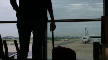 Solo gezgin havaalanı penceresinin yanında bavuluyla bekliyor, pistteki uçaklara bakıyor, macera beklentisini yakalıyor. Gezgin şehveti, havaalanı sahneleri, seyahat anları..