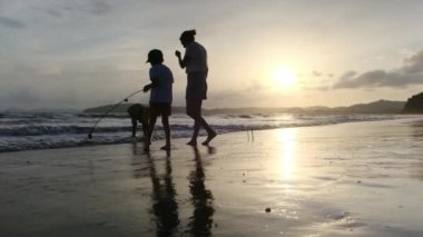 Mutlu anne gün batımında oğullarıyla kıyı şeridinde yürüyor.