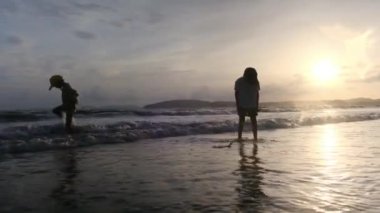 Mutlu anne gün batımında oğullarıyla kıyı şeridinde yürüyor.