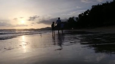 Anne ve oğulları güneşli bir günde deniz kıyısında, gün batımının altında okyanus sahillerinde yürüyorlar..