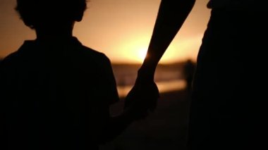 Aile bağının iç açıcı özünü bir anne ve oğlunun silueti gibi huzur dolu bir sahilde büyüleyici bir günbatımının arka planında yaşayın.