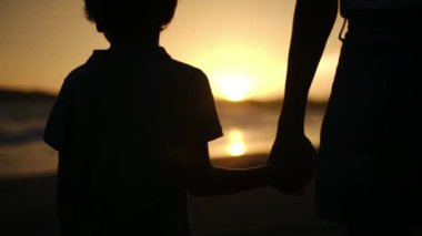 Aile bağının iç açıcı özünü bir anne ve oğlunun silueti gibi huzur dolu bir sahilde büyüleyici bir günbatımının arka planında yaşayın.