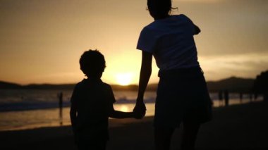 Aile bağının iç açıcı özünü bir anne ve oğlunun silueti gibi huzur dolu bir sahilde büyüleyici bir günbatımının arka planında yaşayın.