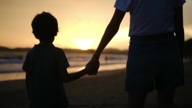 Aile bağının iç açıcı özünü bir anne ve oğlunun silueti gibi huzur dolu bir sahilde büyüleyici bir günbatımının arka planında yaşayın.
