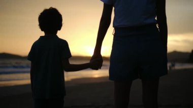 Aile bağının iç açıcı özünü bir anne ve oğlunun silueti gibi huzur dolu bir sahilde büyüleyici bir günbatımının arka planında yaşayın.