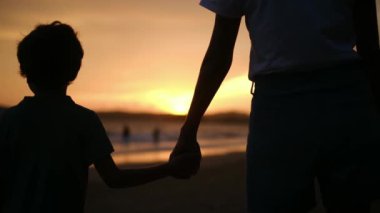 Aile bağının iç açıcı özünü bir annenin ve oğullarının silueti gibi huzurlu bir sahilde büyüleyici bir günbatımının arka planına karşı deneyimleyin.