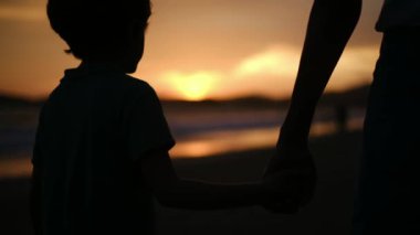 Aile bağının iç açıcı özünü bir annenin ve oğullarının silueti gibi huzurlu bir sahilde büyüleyici bir günbatımının arka planına karşı deneyimleyin.