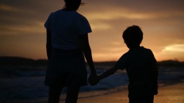 Aile bağının iç açıcı özünü bir annenin ve oğullarının silueti gibi huzurlu bir sahilde büyüleyici bir günbatımının arka planına karşı deneyimleyin.