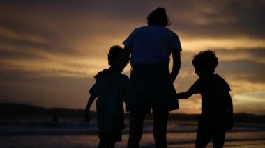 Aile bağının iç açıcı özünü bir annenin ve oğullarının silueti gibi huzurlu bir sahilde büyüleyici bir günbatımının arka planına karşı deneyimleyin.