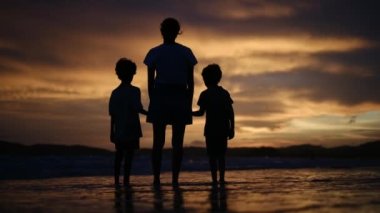 Aile bağının iç açıcı özünü bir annenin ve oğullarının silueti gibi huzurlu bir sahilde büyüleyici bir günbatımının arka planına karşı deneyimleyin.
