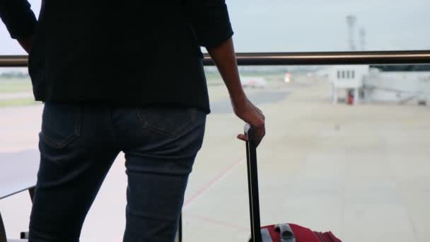 ソロ旅行者は空港の窓からスーツケースで待機し ターマックの飛行機を眺め 冒険の予想を捉えています ウォンダラス 空港のシーン 旅行の瞬間 — ストック動画