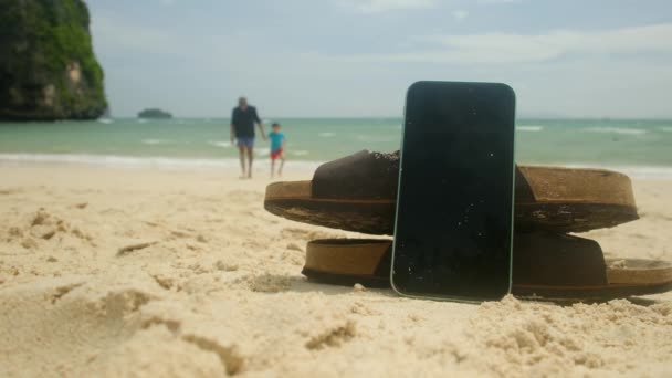 在沙滩上的沙滩背景下 滑行的拖鞋和手机 快乐的假期结束了 — 图库视频影像