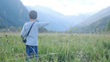 Dağlarda yürüyüş yapan kameralı bir çocuk.