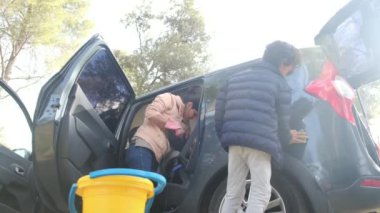 Çocuklar anneleriyle birlikte dikkatli bir şekilde araba temizliyorlar.
