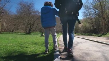 Güneşli bir günde parkta yürüyen bir anne ve oğlu.