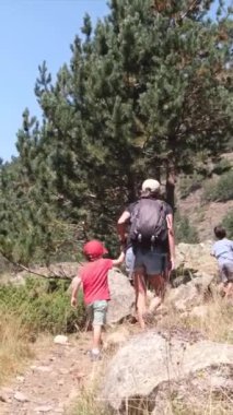 Genç yürüyüş meraklılarıyla güneşli mevsimlerin tadını çıkarın. Oğullarıyla dağlarda yürüyüş yapan bir kadın. 