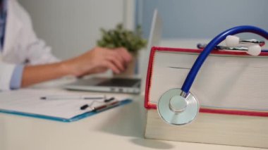 Masadaki kitaplarla steteskopu kapat ve kadın doktor hastanede dizüstü bilgisayarla çalışıyor.