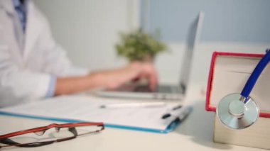 Masadaki kitaplarla steteskopu kapat ve kadın doktor hastanede dizüstü bilgisayarla çalışıyor.