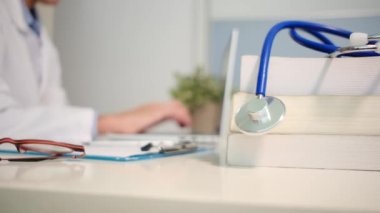 Masadaki kitaplarla steteskopu kapat ve kadın doktor hastanede dizüstü bilgisayarla çalışıyor.