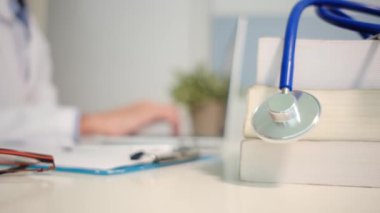 Masadaki kitaplarla steteskopu kapat ve kadın doktor hastanede dizüstü bilgisayarla çalışıyor.