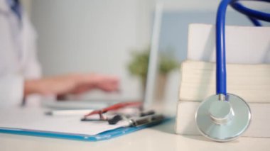Masadaki kitaplarla steteskopu kapat ve kadın doktor hastanede dizüstü bilgisayarla çalışıyor.