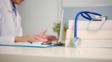 Masadaki kitaplarla steteskopu kapat ve kadın doktor hastanede dizüstü bilgisayarla çalışıyor.