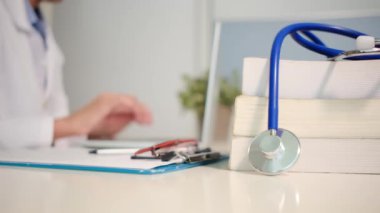 Masadaki kitaplarla steteskopu kapat ve kadın doktor hastanede dizüstü bilgisayarla çalışıyor.