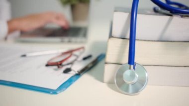 Steteskop manzarasını kapatın. Masada kitaplar ve hastanede arka plan üzerinde çalışan kadın doktor.
