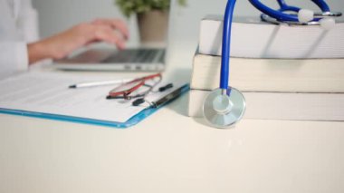 Masadaki kitaplarla steteskopu kapat ve kadın doktor hastanede dizüstü bilgisayarla çalışıyor.