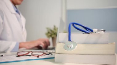 Masadaki kitaplarla steteskopu kapat ve kadın doktor hastanede dizüstü bilgisayarla çalışıyor.