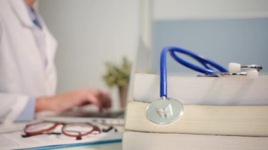 Masadaki kitaplarla steteskopu kapat ve kadın doktor hastanede dizüstü bilgisayarla çalışıyor.