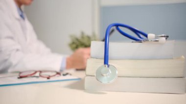 Masadaki kitaplarla steteskopu kapat ve kadın doktor hastanedeki arka planda tablet bilgisayar kullanıyor