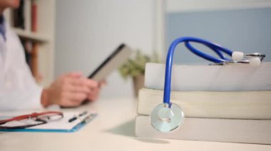 Masadaki kitaplarla steteskopu kapat ve kadın doktor hastanedeki arka planda tablet bilgisayar kullanıyor