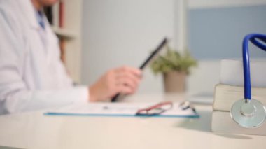 Masadaki kitaplarla steteskopu kapat ve kadın doktor hastanedeki arka planda tablet bilgisayar kullanıyor