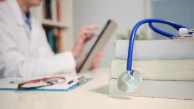 Masadaki kitaplarla steteskopu kapat ve kadın doktor hastanedeki arka planda tablet bilgisayar kullanıyor