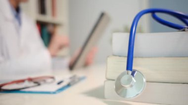 Masadaki kitaplarla steteskopu kapat ve kadın doktor hastanedeki arka planda tablet bilgisayar kullanıyor