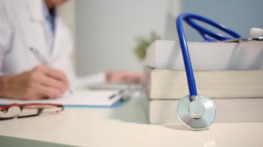 Steteskop manzarasını kapatın. Masada kitaplar ve hastanede arka plan üzerinde çalışan kadın doktor.