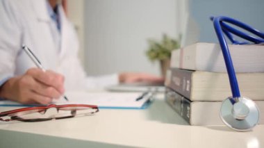 Masadaki kitaplarla steteskopu kapat ve kadın doktor hastanede dizüstü bilgisayarla çalışıyor.