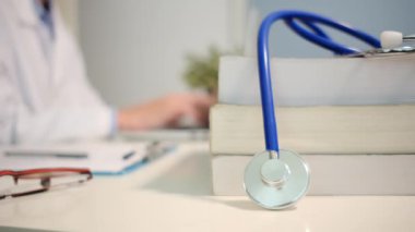Masadaki kitaplarla steteskopu kapat ve kadın doktor hastanede dizüstü bilgisayarla çalışıyor.