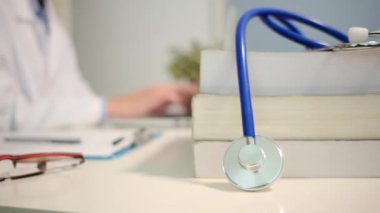 Masadaki kitaplarla steteskopu kapat ve kadın doktor hastanede dizüstü bilgisayarla çalışıyor.