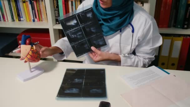 病院のテーブルに座っているX線を示すムスリム心臓科医の近くのビュー — ストック動画