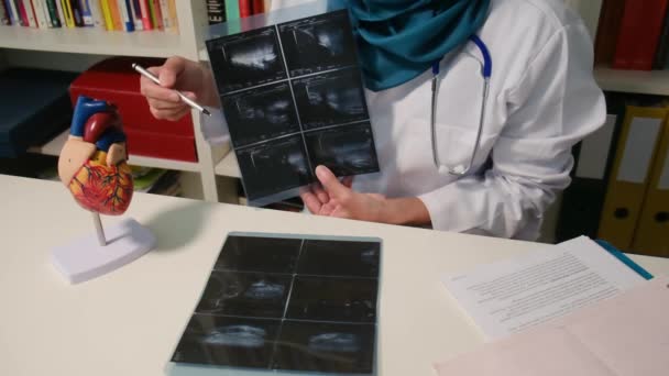 穆斯林心脏科医生坐在医院桌子旁边照X光的近景 — 图库视频影像