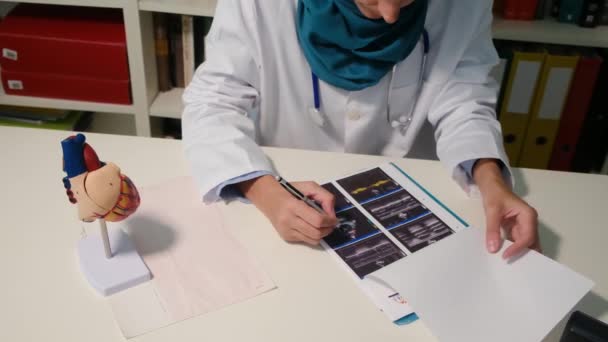 病院のテーブルに座っているイスラム教徒の心臓専門家の近くの眺め — ストック動画