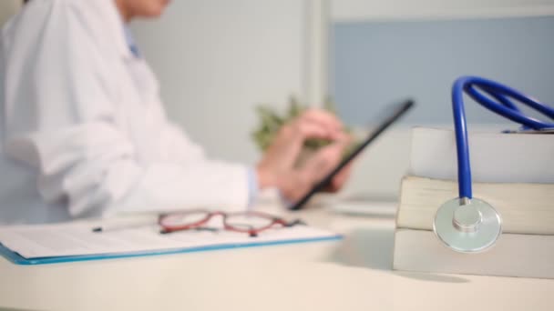 在医院背景下使用平板电脑与桌上书籍和女医生近距离接触听诊器 — 图库视频影像