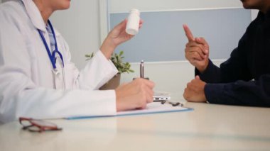 Beyaz üniformalı genç kadın doktoru yakından görüyor ve sağlık kliniğinde masasında oturan erkek hastayla sonuçları ya da belirtileri tartışıyor.