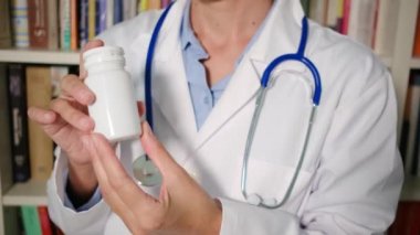 Yakın plan kadın doktor hastanede beyaz önlük giyiyor ve elinde haplar var.