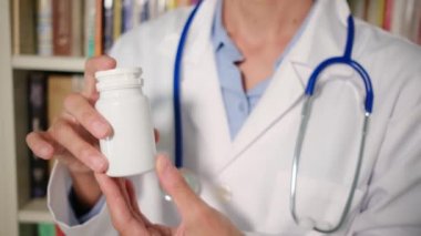 Yakın plan kadın doktor hastanede beyaz önlük giyiyor ve elinde haplar var.
